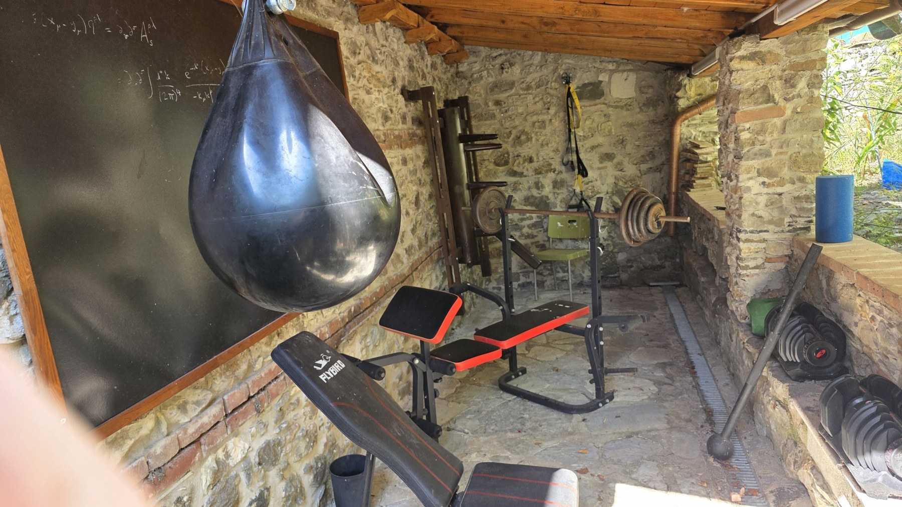 The outdoor Vallico Academy gym under a stone and timber shelter, with weights, a punch bag and a blackboard