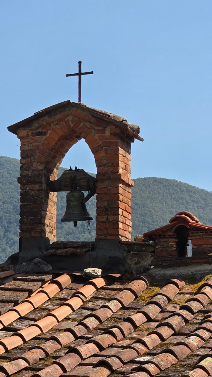 Old bell, brick arch and cross against the mountain